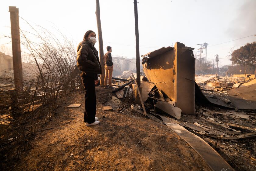 Pacific Palisades, CA - January 08: Ann Tanaka, left, with partner Evan Carlson, right, surveys the damage to her father's home on Swarthmore Ave. in the aftermath of the Palisades fire on Wednesday, Jan. 8, 2025 in Pacific Palisades, CA. (Brian van der Brug / Los Angeles Times)