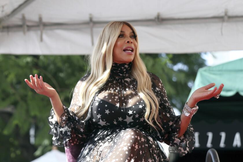 Wendy Williams in a black dress with a star pattern in a shrugging position