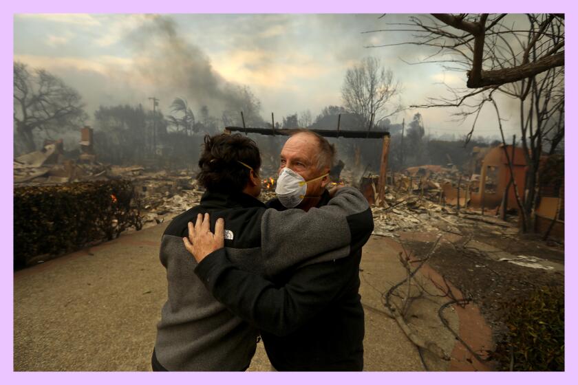 Two humans embrace amid smoldering destruction.