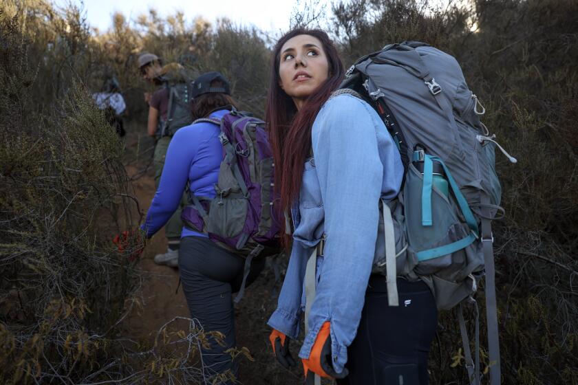 SAN DIEGO, CA - JANUARY 11, 2025: Border Angels safety monitor, Nayely Martinez looks back as she and Border Angels volunteers make their way through thick brush while hiking to make water drops for migrants in the mountains east of San Diego to make water drops for migrants on Saturday, January 11, 2025. (Hayne Palmour IV / For The Los Angeles Times)