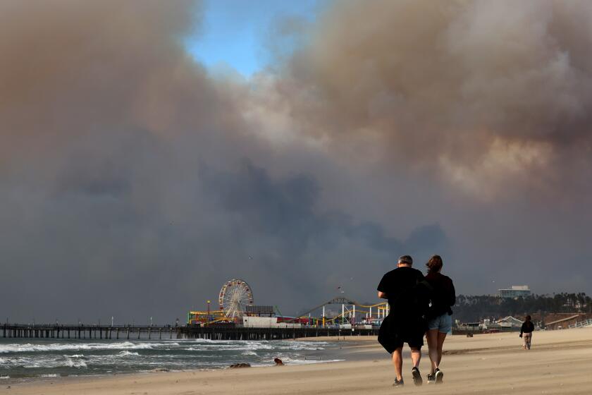 SANTA MONICA, CA, JANUARY 8, 2025: Smoke fills the sky above beachgoers in Santa Monica on Wednesday, January 8, 2025. (Christina House / Los Angeles Times)