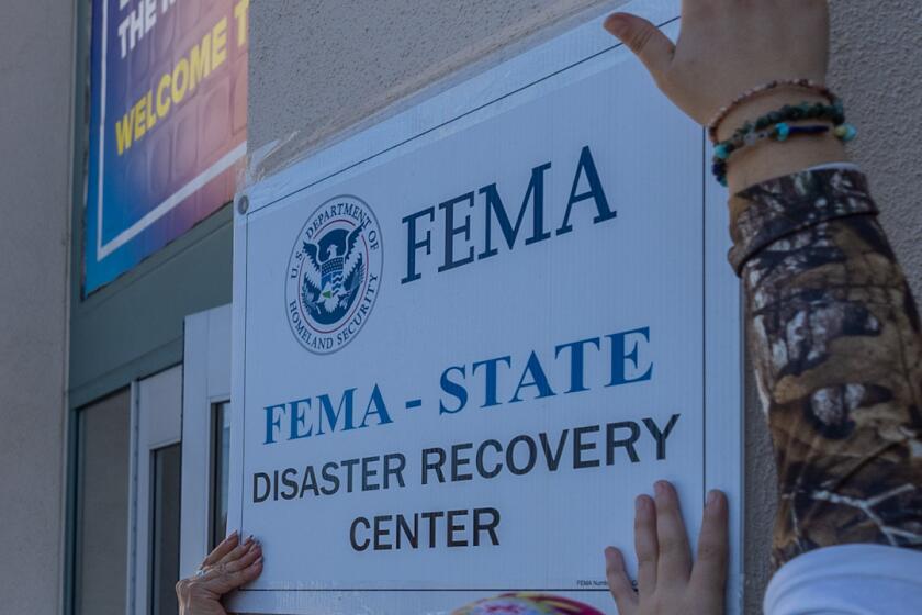 Workers hang up a FEMA disaster recovery center sign.