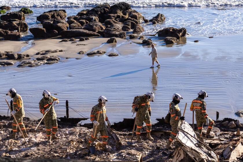 Malibu, CA - January 14: A man walks on the beach as Mexican National Guardsmen help with the grim task of searching for remains in the rubble of a beachfront home on Pacific Coast Highway on Tuesday, Jan. 14, 2025 in Malibu, CA. (Brian van der Brug / Los Angeles Times)