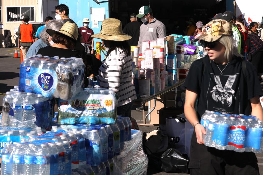 PASADENA, CA - JANUARY 15, 2025 - - Volunteer Sterling Whittaker, 23, right, and other volunteers with National Day Laborer Organizing Network, distribute water, food, clothing, toiletries, diapers and other items for victims of the Eaton fire along East Villa Street in Pasadena on January 15, 2025. (Genaro Molina/Los Angeles Times)