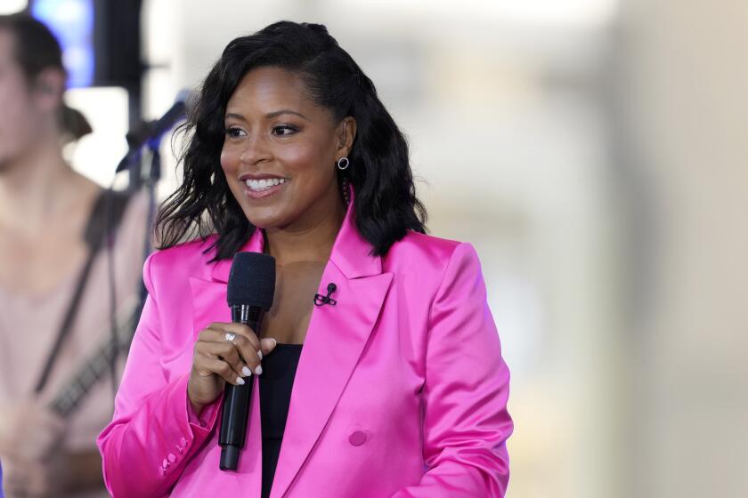 Sheinelle Jones in a hot pink blazer holding a microphone, smiling and looking aside