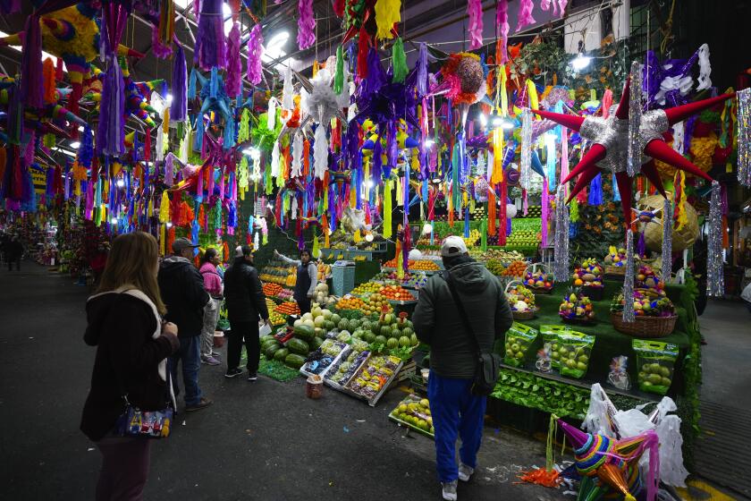 FILE - Christmas piñatas for sale hang over a fruit vendor's stall at the Jamaica market in Mexico City, Dec. 14, 2023. (AP Photo/Fernando Llano, File)