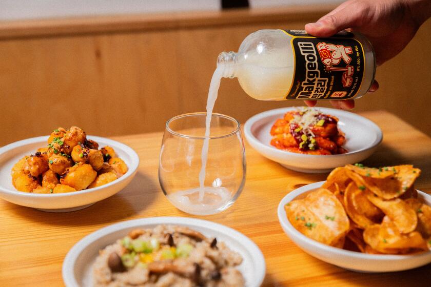 A hand pours from a bottle of makgeolli into a glass, with food items from Jilli.