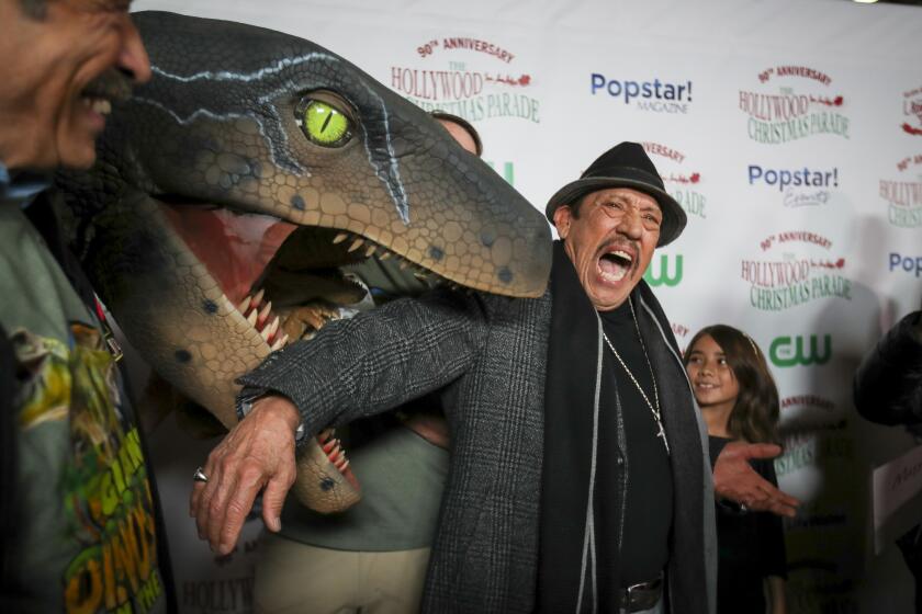 Hollywood, CA - November 27: Actor Danny Trejo, center, who served as grand marshal of the parade, plays around with a dinosaur from DINOSAURS IN THE VALLEY exhibit at Pierce College in Woodland Hills, on the Red Carpet at The 90th anniversary Hollywood Christmas Parade in Hollywood Sunday, Nov. 27, 2022. (Allen J. Schaben / Los Angeles Times) Actor Danny Trejo served as grand marshal of the parade, which will also feature dozens of movie and TV stars and other celebrities, movie and novelty cars, balloons, marching bands and city officials. Parade hosts include Erik Estrada, Laura McKenzie, Dean Cain, Montel Williams, special co-host Elizabeth Stanton.