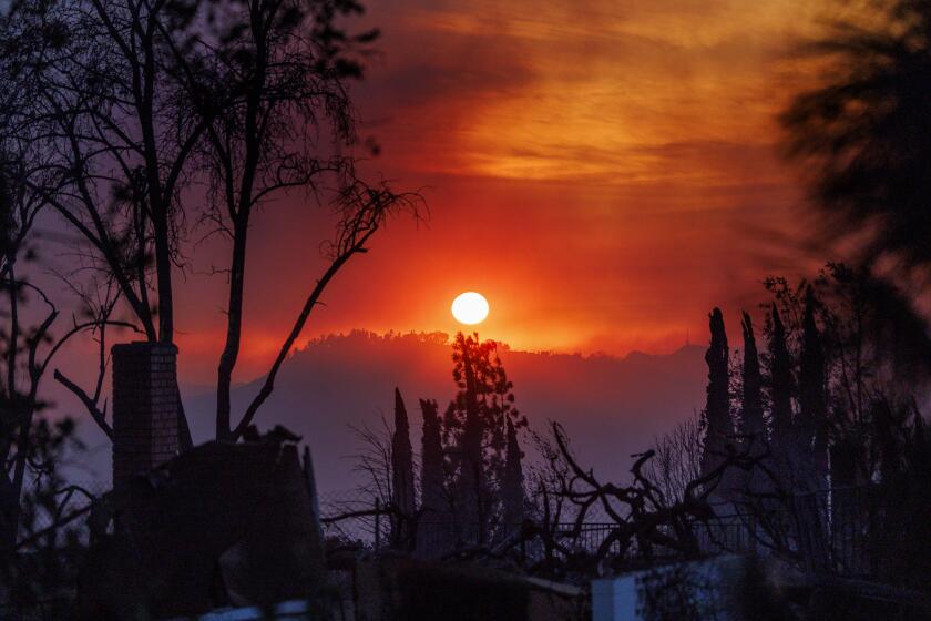 ALTADENA, CA - JANUARY 8, 2025: A smoky haze fills the dusk landscape as a home smolders in the foreground during the Eaton fire on January 8, 2025 in Altadena, California. (Gina Ferazzi / Los Angeles Times)